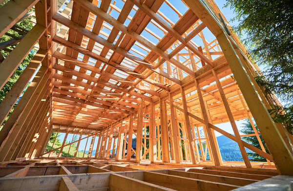Under-construction residential wooden frame home located near a forest. Commencement of a new construction project for a cozy house or a mountain cottage. Idea of contemporary ecological construction.