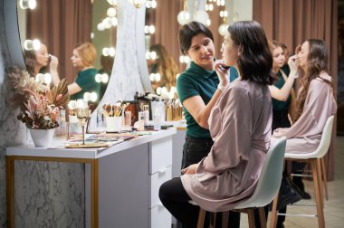 Profesyonel makyaj sanatçısı. Stüdyoda müşteri için makyaj yapıyor. Kadın güzellik uzmanı kadın yüzüne fondöten sürerken karıştırıcı sünger kullanıyor..