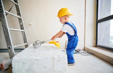 Ev tadilatı yaparken inşaat aleti kullanan bir sürü inşaat işçisi. İş tulumları ve güvenlik kaskı giyen çocuk tamir ve yenileme işleri için malzeme hazırlıyor..