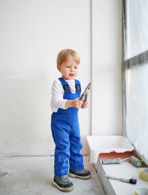 Çocuk inşaat işçilerinin elinde pense var. İş yerindeki çocuk, pencerenin önünde duruyor ve tadilatta. Ev yenileme, tamir işleri ve çocukluk kavramı.
