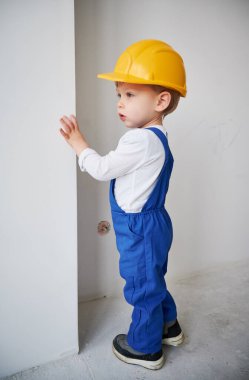 Çocuk inşaat işçisi, evin duvarının yanında, tadilatta. Kasklı ve iş tulumlu çocuk gelecekteki evde oynuyor..