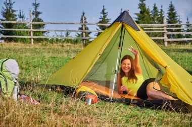 Kamp yapan bir kadın. Yazın seyahat eden çekici, sportif bir turist. Güzel, genç bir bayan çadırda uzanıyor, ara veriyor, kameraya bakıyor. Turizm ve yürüyüş kavramı.