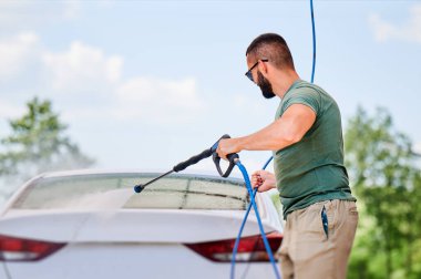 Açık hava yıkamada su tabancasıyla lüks araba yıkamak. Kendine güvenen bir adam arabasını yüksek basınçlı su jetiyle temizliyor. Teknik servis kavramı.