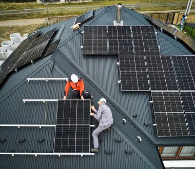 Fotovoltaik güneş panellerini mezurayla ölçen işçiler. Erkekler fotovoltaik etkiyle elektrik üretmek için evin çatısına güneş modülü monte etmeden önce ölçüm yapıyorlar. Hava görünümü