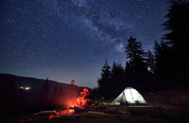 Geceyi dağlarda kamp yaparak geçiririz. Erkek ve kadın, ateşli kaşifler, Chumack Patikası 'nın nefes kesen güzelliğinin altında, yemyeşil bir çadırı olan titreyen ateşle rahatlarlar..