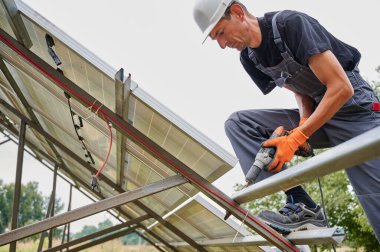 Güneş panelleri için elektrikli matkapla metal kirişleri tamir eden bir işçi. Yenilenebilir ve ekolojik enerji kavramı. Modern teknoloji ve yenilik.