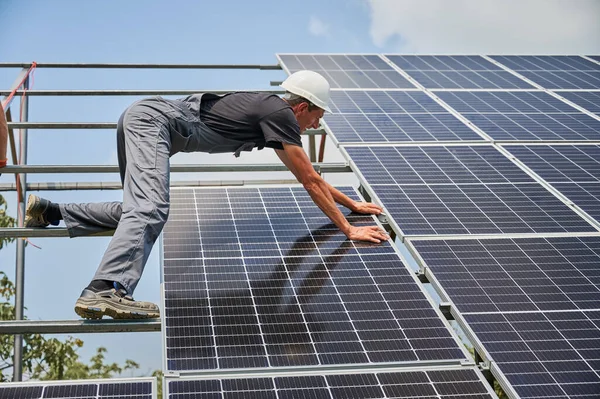 stock image Male worker buildingg photovoltaic solar panel system outdoors. Man electrician placing solar module on metal rails, wearing construction helmets. Renewable and ecological energy.