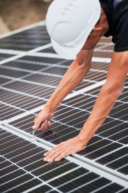 Adamın biri fotovoltaik güneş modüllerini evin çatısına monte ediyor. Kasklı elektrikçi uğursuz anahtarın yardımıyla güneş paneli sistemi kuruyor. Alternatif ve yenilenebilir enerji kavramı.