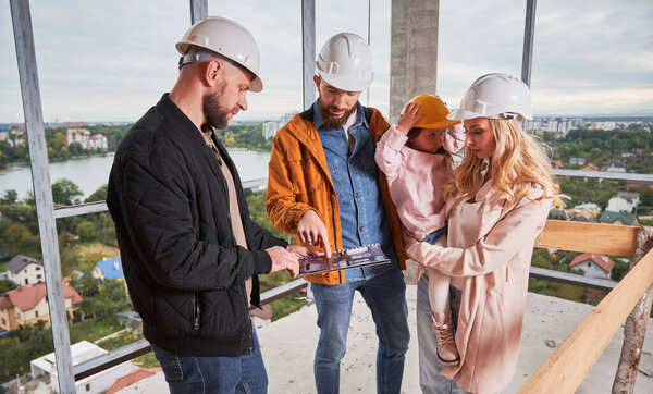 Man and woman looking at catalogue while choosing interior design for new apartment with building worker. Couple with child planning home construction and redesigning with specialist.