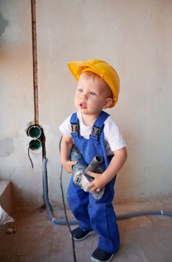 Elektrikli öğütme makinesi tutan sevimli bir inşaat işçisi. Evde tadilat sırasında iş tulumu ve güvenlik kaskı takan sevimli bir çocuk..
