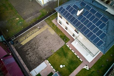 Çatıda fotovoltaik güneş paneli modülleri olan otonom bir evin havadan görüntüsü. Dışarıda güneş enerjisi, çimenlik ve asfalt sistemi olan bir ev. Yenilenebilir enerji ve konut kavramı.