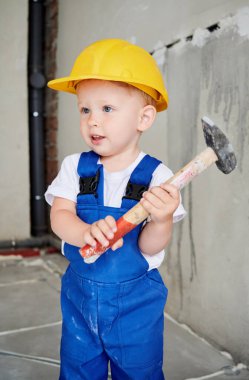 Çekiç yapım aletini tutan sevimli çocuk inşaat işçisi. Güvenlik kaskı takan ve tadilat sırasında evde poz veren sevimli bir çocuk..