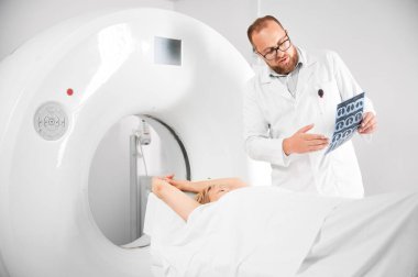 Tıbbi bilgisayarlı tomografi ya da MRI tarayıcısı. Doktor MRI sonuçlarını tutuyor ve açıklıyor. Kanepede yatan kadın hasta. Tıp, sağlık ve modern teşhis kavramı.