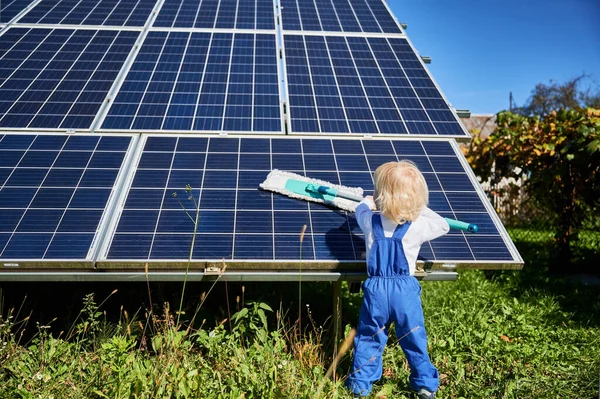 Small boy learning how to care about solar panels. Back view of young kid cleaning new solar battery at warm sunny day. Concept of young generation and alternative energy.