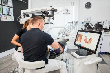 Dentist scanning patients teeth with modern machine for intraoral scanning. Digital print of patients teeth is on big screen. Modern high precision technologies. Concept of modern dentistry