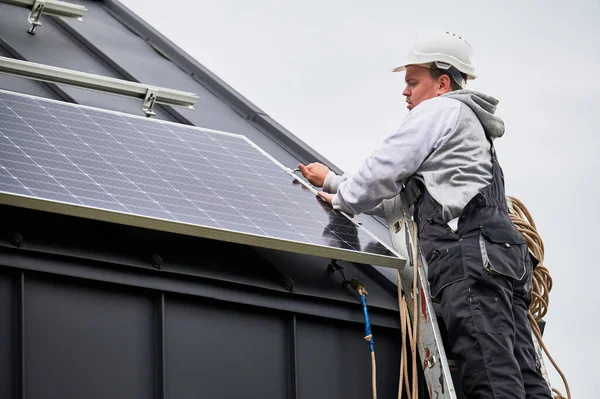 Stock image Man installer mounting photovoltaic solar panels on roof of house. Engineer in helmet installing solar module system with help of hex key. Concept of alternative, renewable energy.