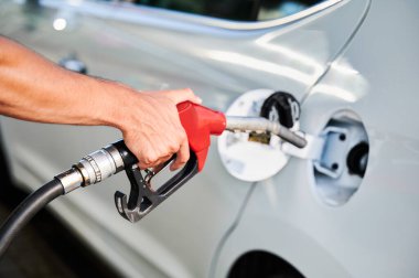 Close up view of man refueling car gas tank. Driver holding red pump nozzle and filling gas tank. Pumping gasoline fuel in car at petrol station. clipart