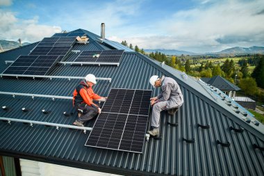 Çatıda fotovoltaik güneş modülü istasyonu inşa eden çatıcılar. Miğferli elektrikçiler güneş paneli sistemi kuruyor. Alternatif ve yenilenebilir enerji kavramı. Hava görünümü.