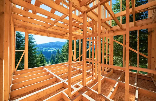 Wooden frame house under construction near forest. Beginning of new construction of cozy house on the edge of forest in mountains. Concept of modern ecological construction and modern architecture.