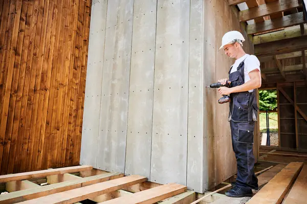 Marangoz ahşap çerçeveli ev inşa ediyor. Evin ön cephesini çimento parçacıkları ile kaplayan işçi onları tornavidayla bağlıyor. Modern çevre dostu yapı kavramı.