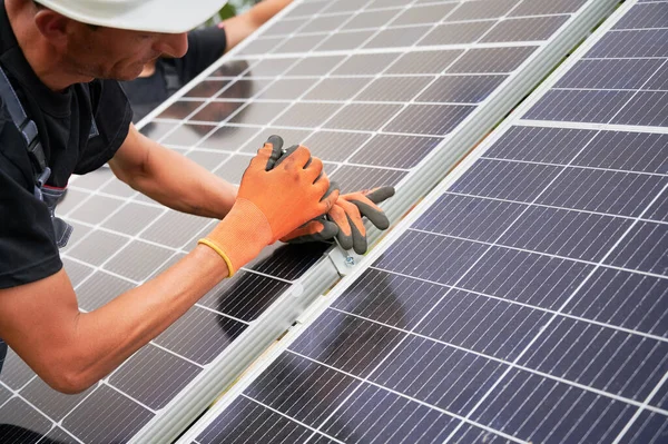 Close up of man solar installer mounting photovoltaic solar panel outdoors. Male technician in safety construction helmet assembling solar modules. Concept of alternative energy sources.