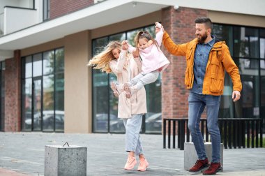 Sakallı bir adam ve sarışın bir kadın kucağında küçük bir kız ve caddede yürürken gülümsüyor. Çocuklar dışarıda eğlenirken mutlu ve sevgi dolu bir aile.