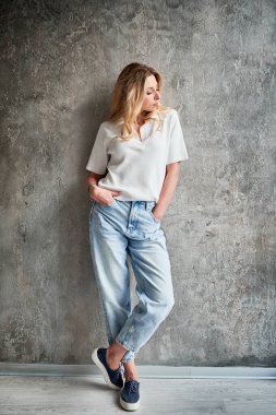 Yeni dairenin duvarında duran, günlük kıyafetli bir kadın. Kadın elini kot pantolonunun cebine sokuyor...