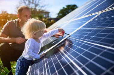 Man showing his small child the solar panels during sunny day. Father presenting to son modern energy resource. Little steps to alternative energy.