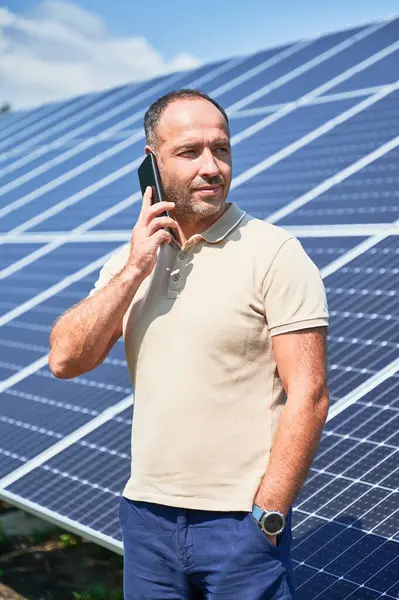 Confident businessman having important call. Man talking about his investment in alternative energy resource. Man taking on phone on background of solar panels.