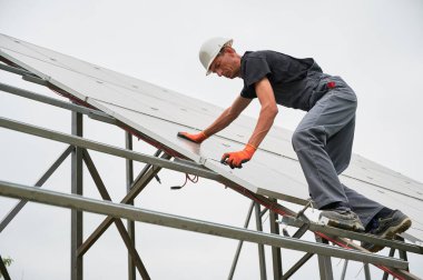 Fotovoltaik güneş panelleri inşa eden adam teknisyen. Güvenlik kasklı erkek işçi fotovoltaik panel sistemi monte edilirken güneş modülünü destekleyen yapıya sabitliyor.