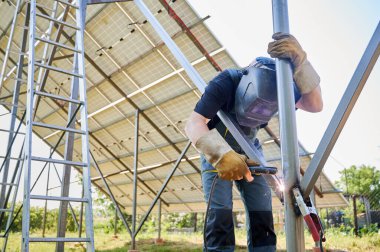 Kaynak makinesi ile kaynak yapan kaynak makinesi güneş panelleri için. Koruyucu kaynak kask giyen, iş kıyafeti giyen, bulanık arka planda güneş istasyonu üzerinde çalışan bir işçi..