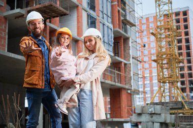 Erkek, kadın ve çocuk inşaat halindeki binanın dışında duruyor. İnşaat alanında sokakta poz veren mutlu aile sahipleri..