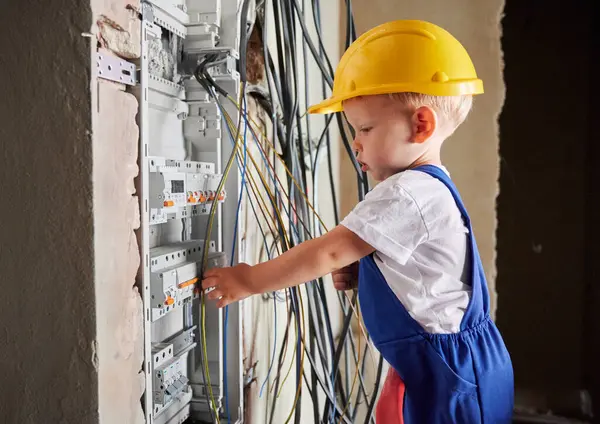 Side view of child fixing electrical switchboard or distribution board in apartment under renovation. Boy electrician repairing household electrical panel with automatic fuses.