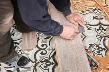 Kaplama tahtaya düz çizgi çizerken metal cetvel ve kalem kullanarak erkek inşaat işçilerinin etrafını sarın. Adam zemin kurulumu için kaplama paneli hazırlıyor. Döşeme yenileme kavramı.