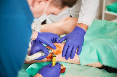 Dizinde iğne yapan doktorlara ve hastanede ultrason taramasına yakından bakın. Cüppeli, lateks eldivenli, dizlerini tutan adamlar. Tıp kavramı ve sağlıkla ilgilenmek.