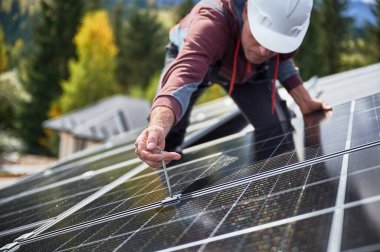 Elektrikçi adam evin çatısına fotovoltaik güneş panelleri monte ediyor. Başlıktaki mühendis, uğursuz anahtarın yardımıyla güneş modülü sistemi kuruyor. Alternatif, yenilenebilir enerji kavramı.