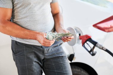 Adam yakıta harcayacak parayı sayıyor. Ulaşım masrafları konsepti. Yakıt ikmali arabasının arka planında dolar sayan adam manzarası.