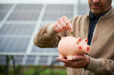 Erkek yatırımcı parasını alternatif enerjiye yatırıyor. Piggy Box 'a bozuk para koyan adamın yakın görüntüsü. Doğayı kurtararak para kazanıyorlar..