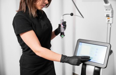 Doktor Güzellik Uzmanı cilt yenileme prosedürü için radyoterapi cihazı kullanıyor. Kadın kozmetolojist güzellik kliniğinde modern kozmetoloji ekipmanlarına dokunuyor.