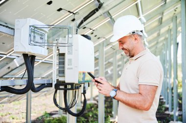 Güneş panelini fırlatma konusunda hevesli bir adam. Gülümseyen işçi iyi iş çıkardığını bildiriyor. Miğferli bir adam telefonuyla PV bataryasının arka planında mesaj atıyor..