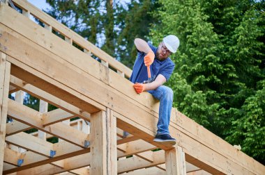 Ahşap işçisi ormanın yanına iki katlı kereste çerçeveli bir ev inşa ediyor. Sakallı adam, güvenlik kaskı takılı bir şekilde yapıya çivi çakıyor. Çağdaş ekolojik yapı kavramı.