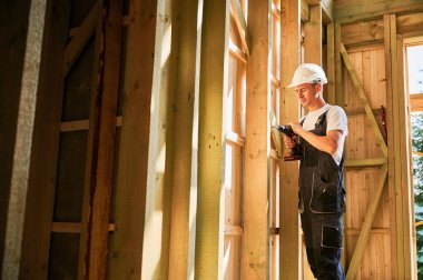 Marangoz ahşap çerçeveli ev inşa ediyor. Tornavidayla çalışan, iş tulumu ve kask giyen bir adam. Modern çevre dostu yapı kavramı.