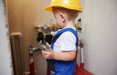 Çocuk boru ve termometre göstergesi ile tesisat kurulumunu tamir ederken ingiliz anahtarı kullanıyor. Tesisatçı çocuk tadilat altındaki evde tesisat borularını tamir ediyor..
