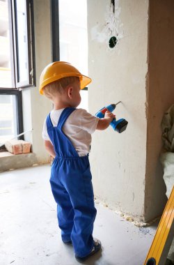 Çalışan bir çocuk, tadilat sırasında evde oyuncak elektrikli matkapla duvarı deliyor. Güvenlik kasklı çocuk, apartman tadilatında çalışırken sondaj aleti kullanıyor..