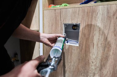 Silikon dolgu maddesini sifon panelinin köşelerine uygulayan tesisatçıya yaklaş. Tadilat aşamasındaki daireye hijyenik tuvalet sifonu sistemi kurarken tesisat aleti aplikatörü kullanan bir adam..