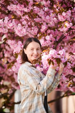 Alerjisi olan bir kadın, bahardaki sezonluk alerjiden zevk alıyor. Baharda çiçek açan sakura ağacının önünde gülümseyen güzel bir kadının portresi. Bahar alerjisi konsepti.