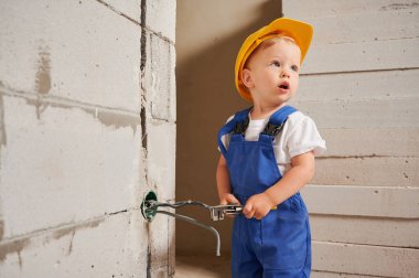 Duvara elektrik kablosu ve soket yerleştirirken tel kesici kullanan sevimli bir çocuk inşaat işçisi. Güvenlik kasklı bir çocuk, tadilat altındaki dairede elektrik kabloları monte ediyor..