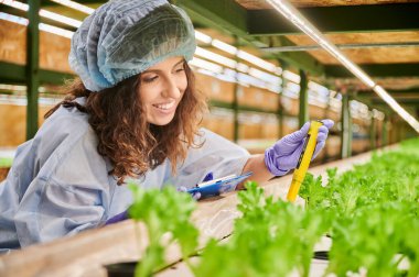 Serada pH ölçer kullanan kadın bilim adamı. Neşe dolu kadın bahçıvan elinde pano tutarken ve gülerken toprağın pH değerini dijital elektronik cihazla ölçerken.