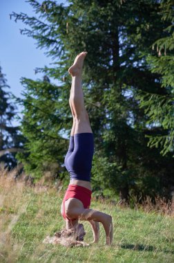 Kadın dışarıda sabah egzersizi yapıyor. Çimlerin üzerinde duran esnek bir kadın. Sıska bir kadın spor giyer, yoga yapar, meditasyon yapar, dışarıda antrenman yapar. Yoga ve spor kavramı.