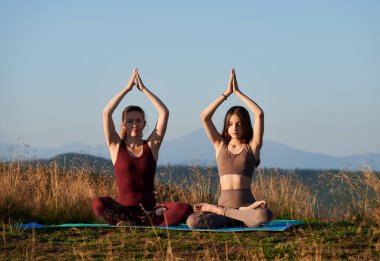 Dağlarda yoga yapan iki kız. Sabahın erken saatlerinde meditasyon. Anne ve kızı nilüfer pozisyonunda oturuyor ve ellerini kaldırmış dağların arkasında..